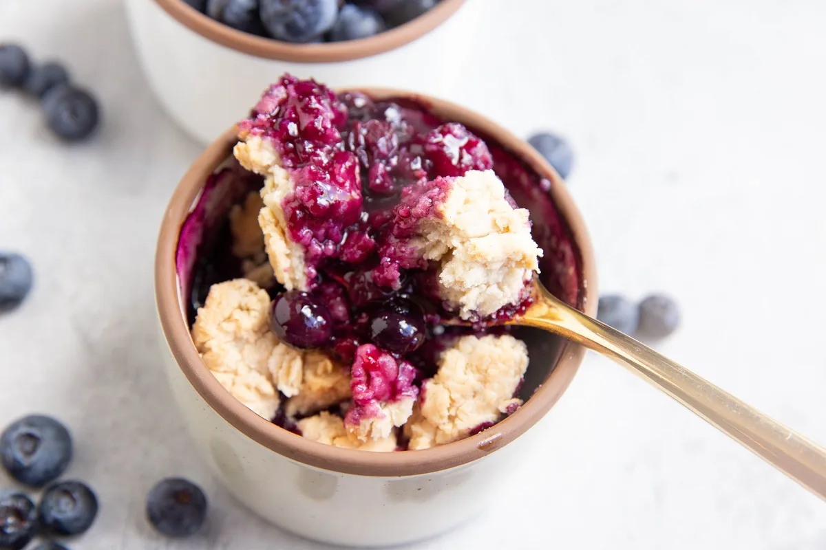 Gold spoon taking a bite out of a single serving of blueberry cobbler