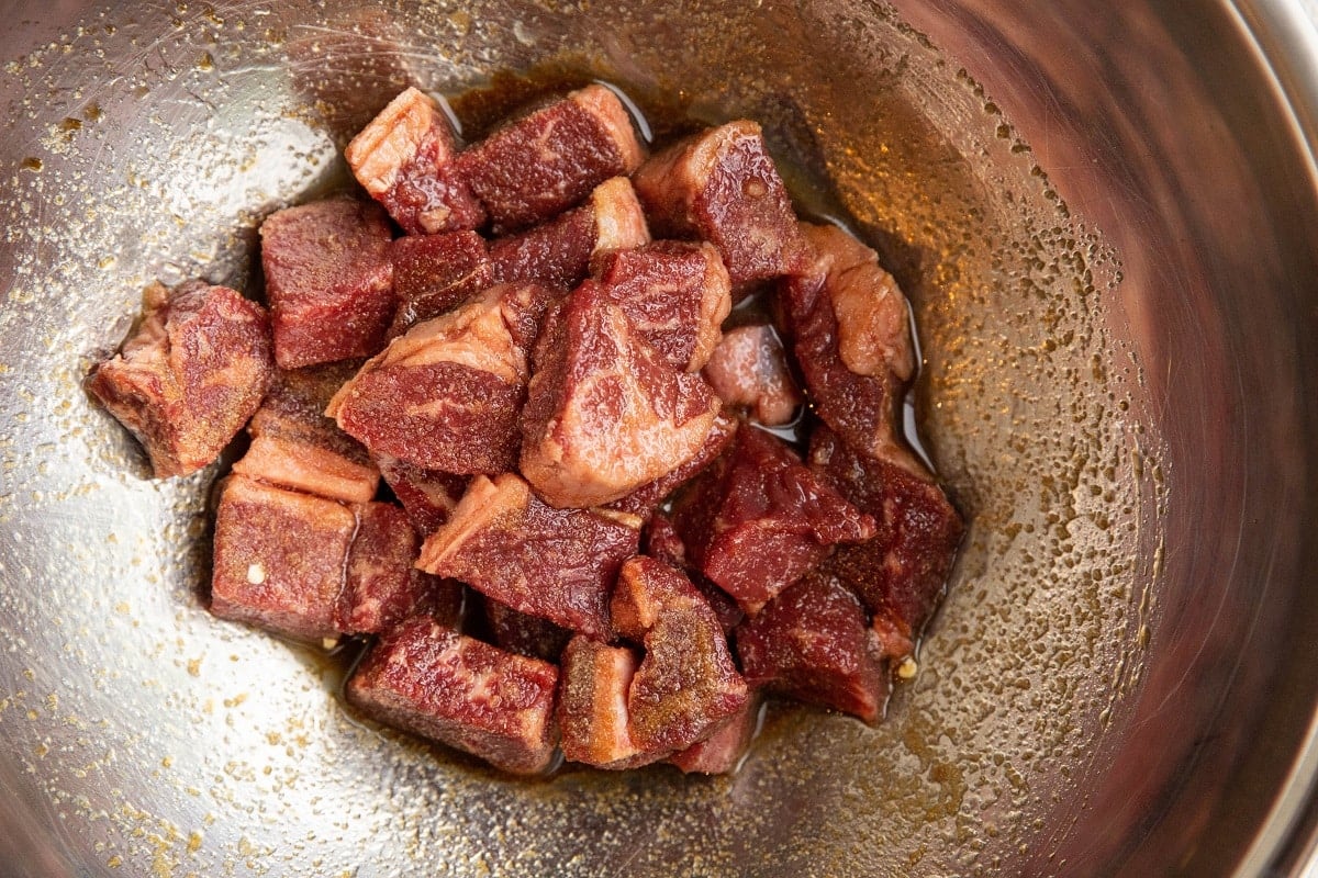 Cubes of beef in a mixing bowl with steak marinade.