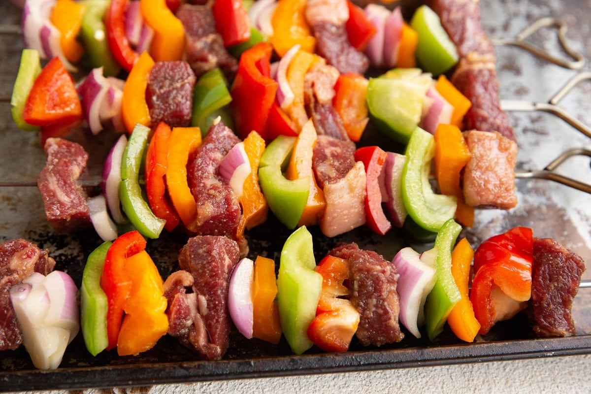 Raw beef kabobs on a baking sheet, ready to be grilled