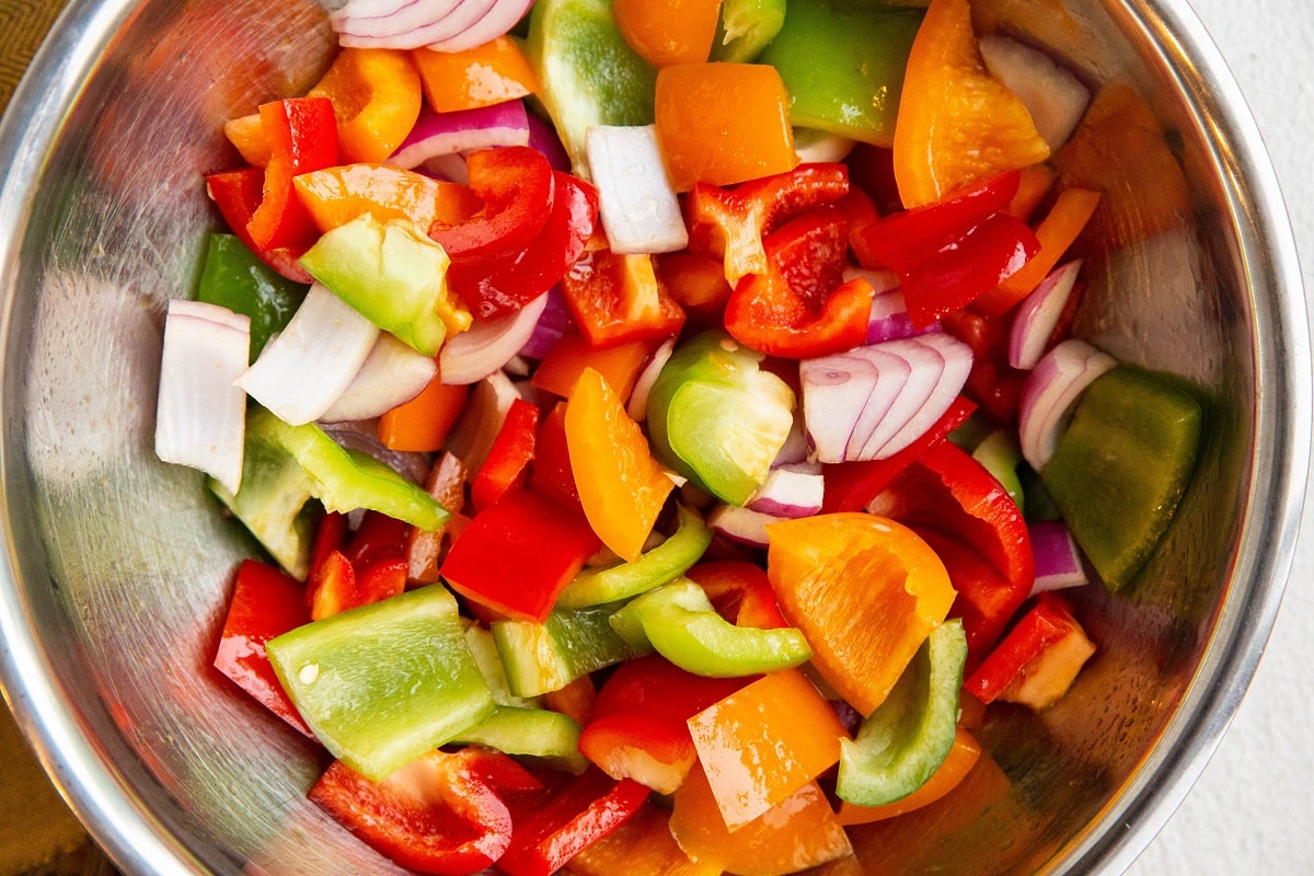 Mixing bowl with chopped peppers and onions inside, to be used for skewers.