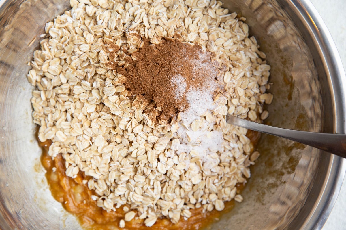 Mixing bowl with mashed banana, almond butter and pure maple syrup mixed together and oats, cinnamon and salt on top.