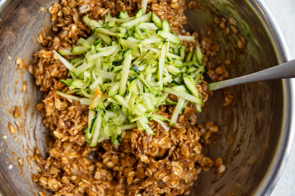 oatmeal cookie dough in a mixing bowl with shredded zucchini being added in.