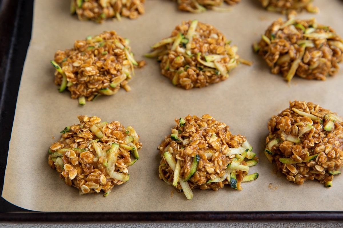 Mounds of zucchini oatmeal cookie dough on a parchment-lined cookie sheet.