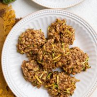 Two white plates of zucchini oatmeal cookies with a golden napkin and a fresh zucchini to the side.