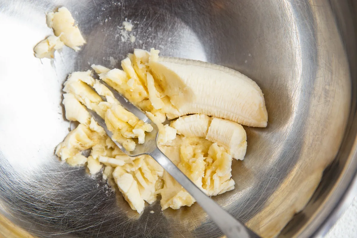 Fork mashing a banana in a mixing bowl.