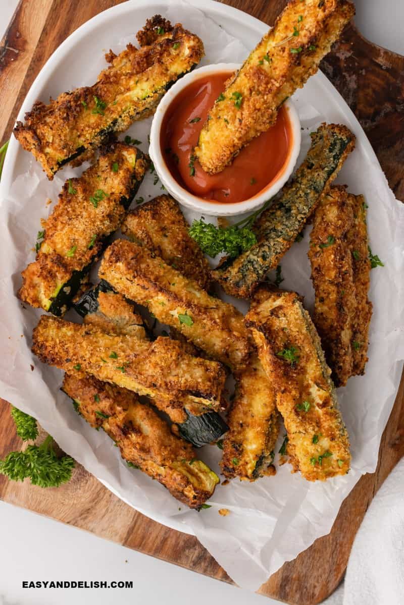 Cooked breaded zucchini on a plate with a dipping sauce.