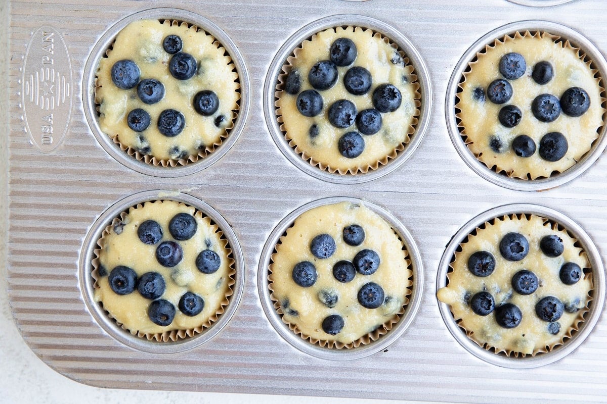 Muffin tin lined with muffin papers, filled with blueberry muffin batter, ready to go into the oven.