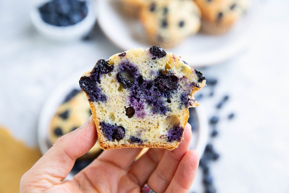 Hand holding a blueberry muffin that has been sliced in half so you can see the inside.