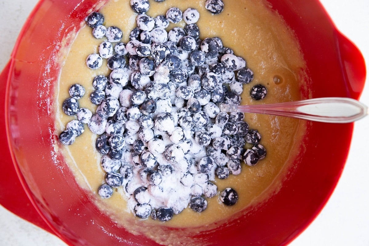 Muffin batter in a red mixing bowl with blueberries on top.