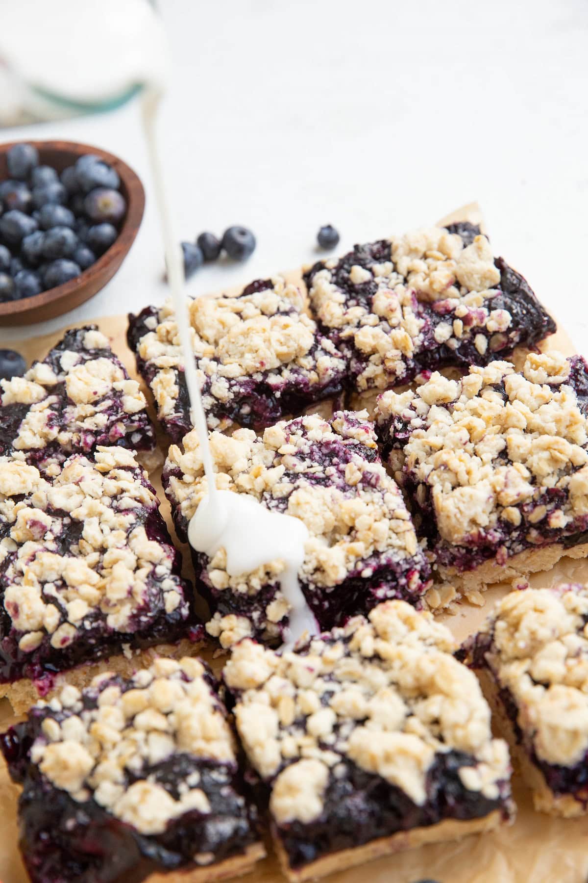 Drizzling powder sugar glaze on top of blueberry crumb bars.