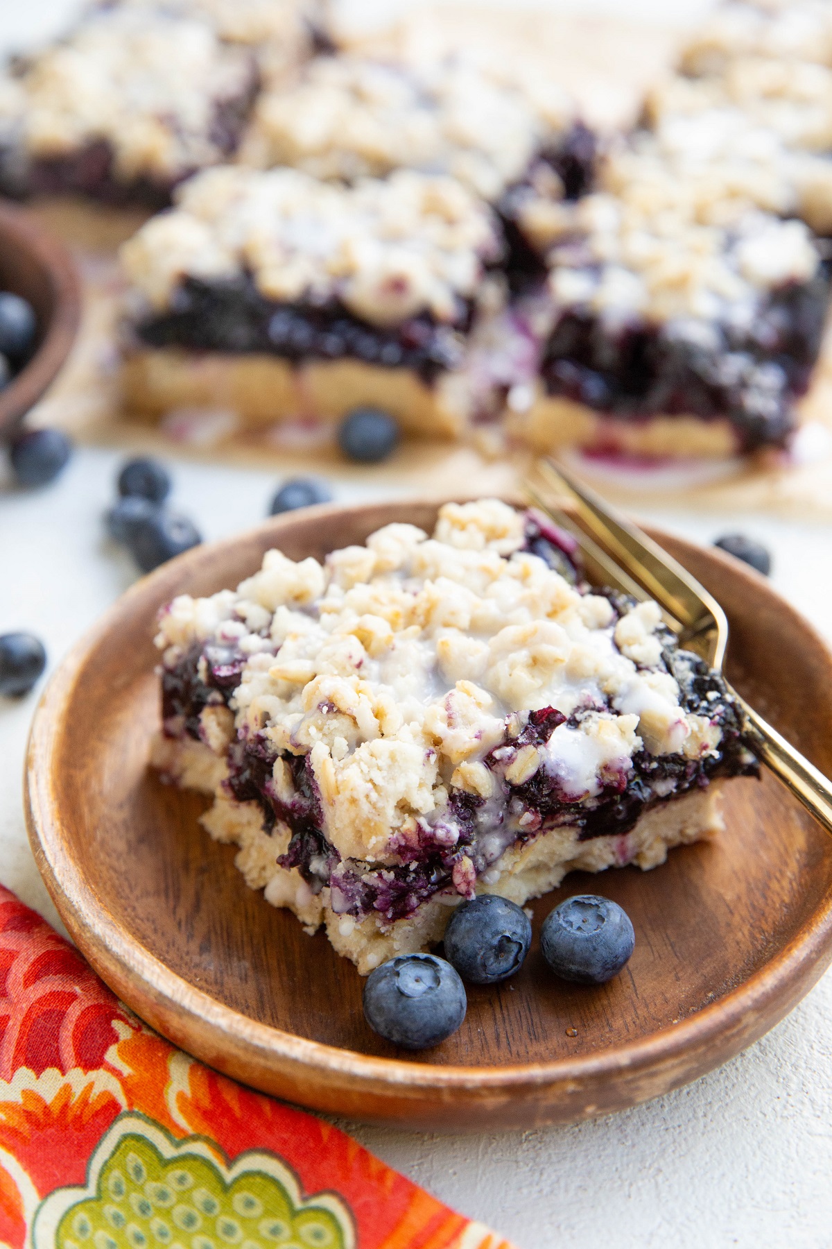 Blueberry crumb bar on a wooden plate with a golden fork and blueberries