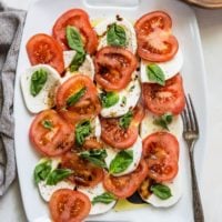 White serving platter of caprese salad with a wooden plate and a serving fork.