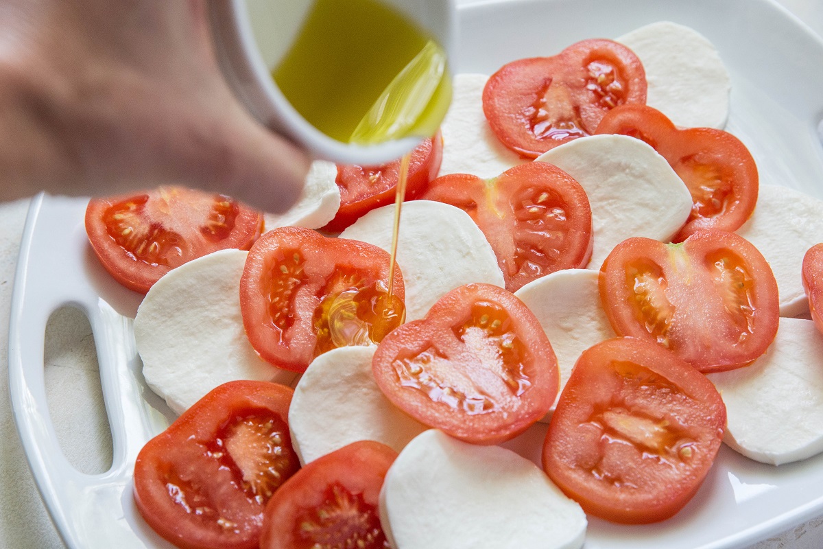 Pouring olive oil over slices of tomatoes and mozzarella cheese