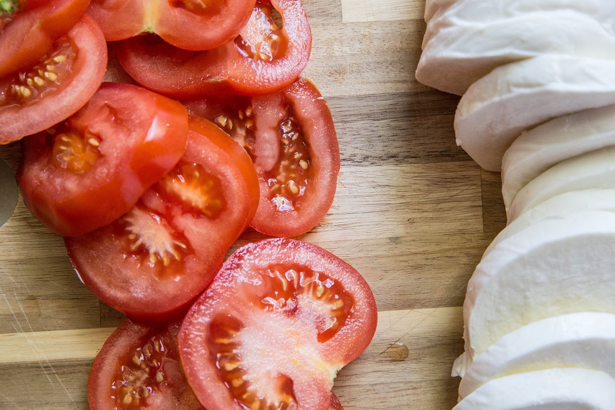 Sliced tomatoes and sliced mozzarella on a wooden cutting board.