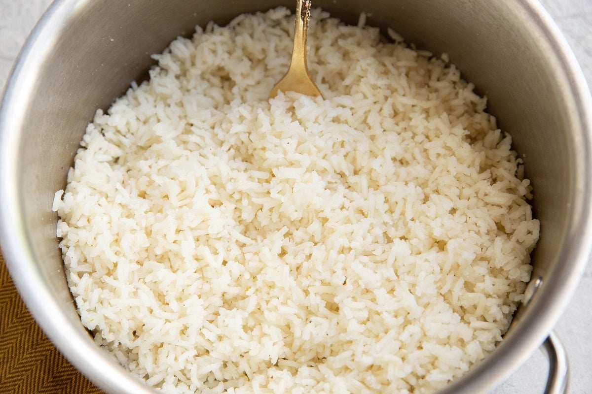 Cooked white rice in a saucepan with a golden fork fluffing it.