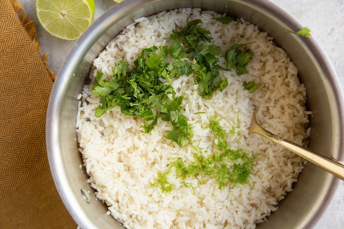Fresh cilantro and lime zest on top of cooked white rice, ready to be mixed in.