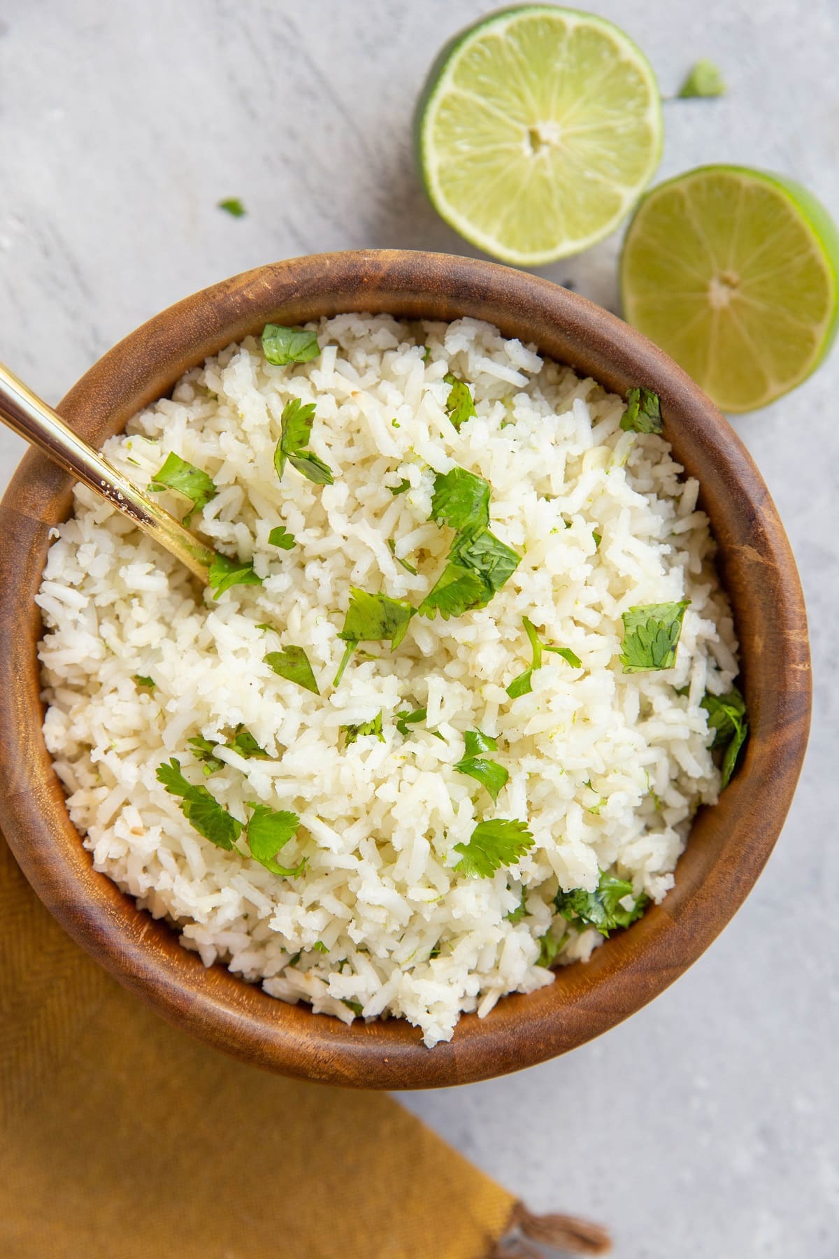 Cilantro rice in a wooden bowl with limes to the side and a golden spoon, ready to serve.