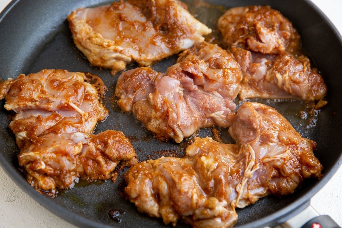 Skillet full of chicken thighs, cooking.