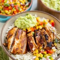 Chicken burrito bowl with corn salsa and guacamole in the background.