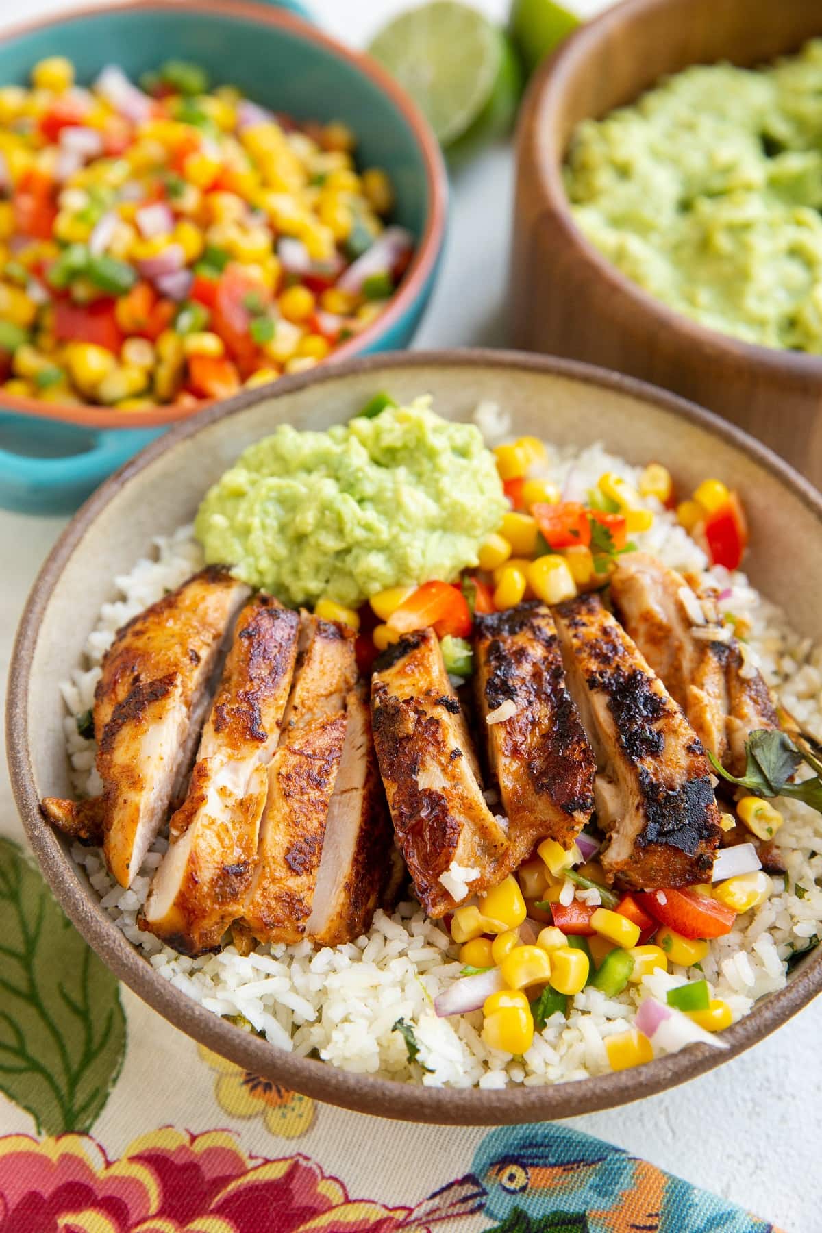 Chicken burrito bowl with corn salsa and guacamole in the background.