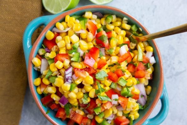 Corn salsa in a blue serving bowl with a gold spoon.