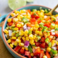 Blue bowl full of corn salsa with a fresh lime in the background.