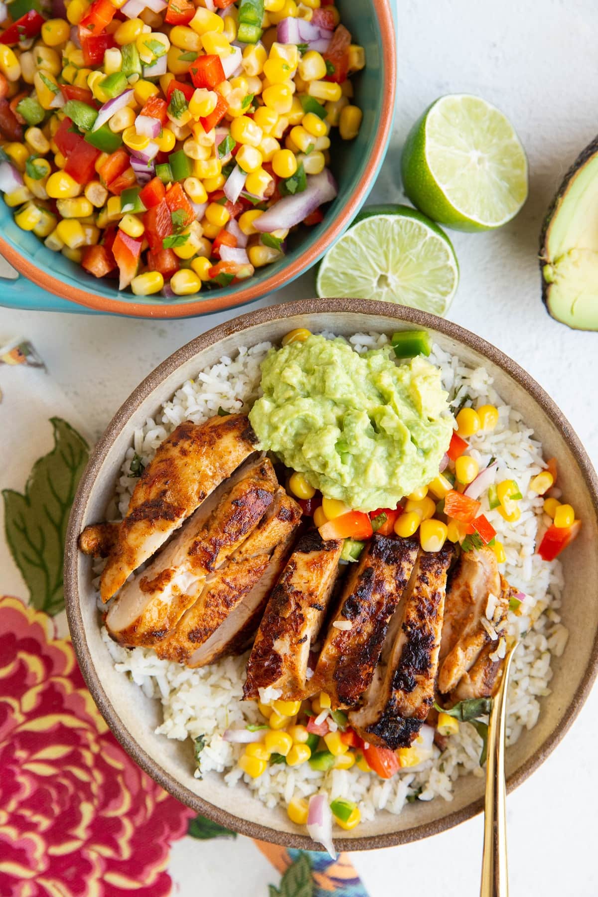 Burrito bowl with chicken, corn salsa and guacamole inside of it with a bowl of corn salsa to the side.