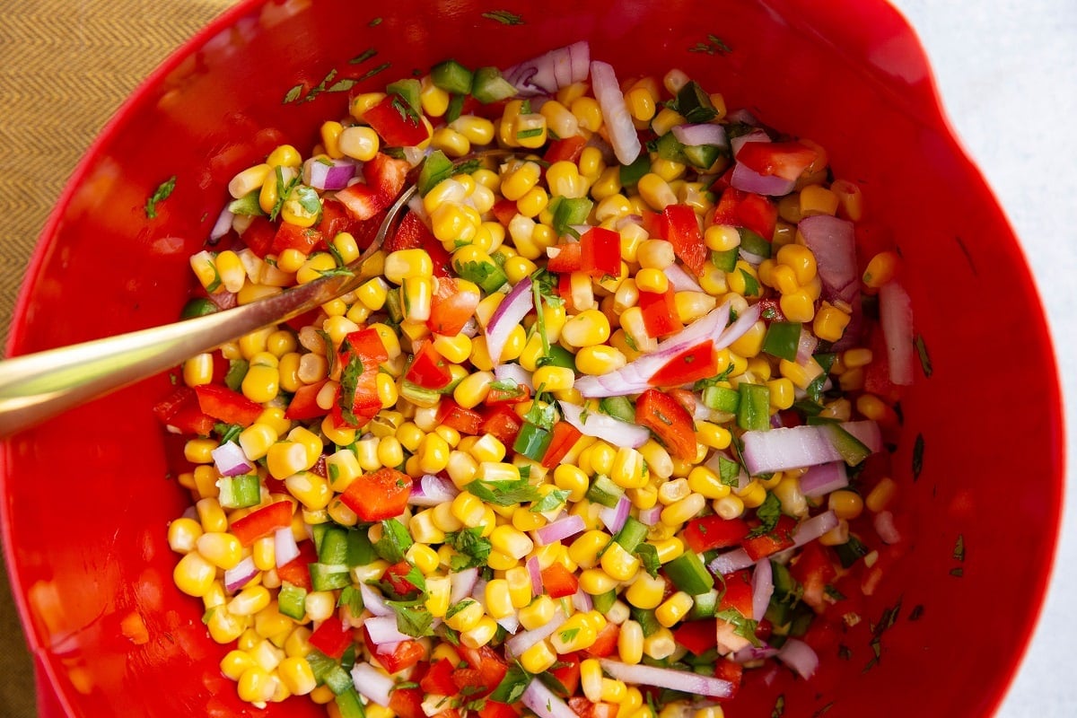 Corn salsa mixed up in a red mixing bowl, ready to serve.