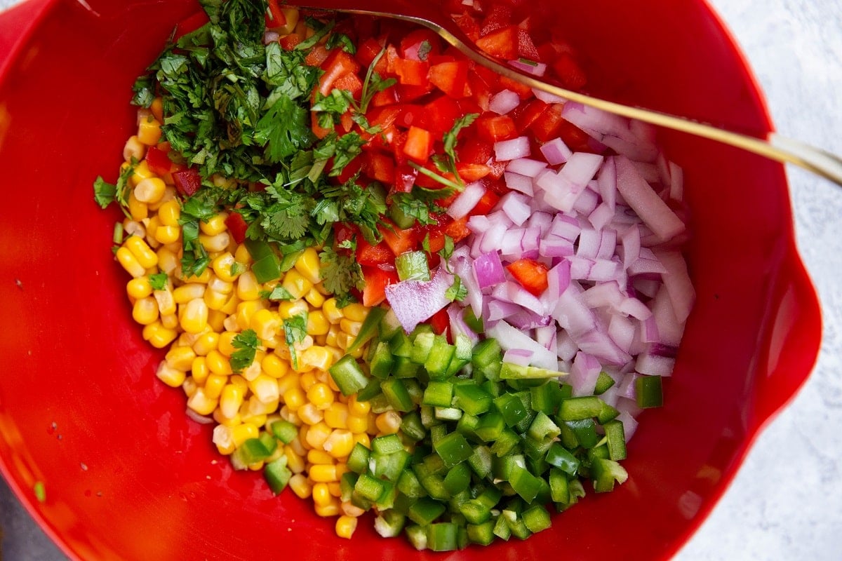 Red mixing bowl full of corn salsa ingredients