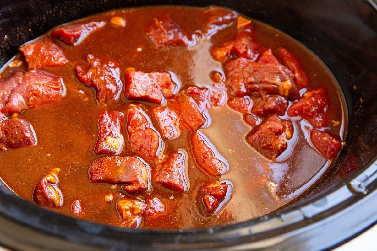 Stew meat and chile colorado sauce in a crock pot, ready to be slow cooked.