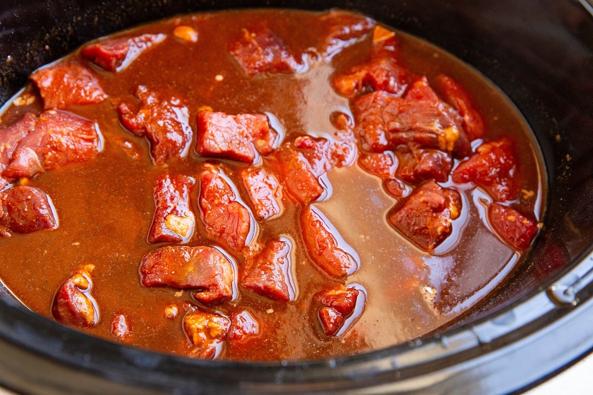 Stew meat and chile colorado sauce in a crock pot, ready to be slow cooked.