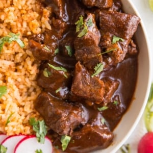 Chile Colorado in a white bowl with Mexican rice for the perfect meal.