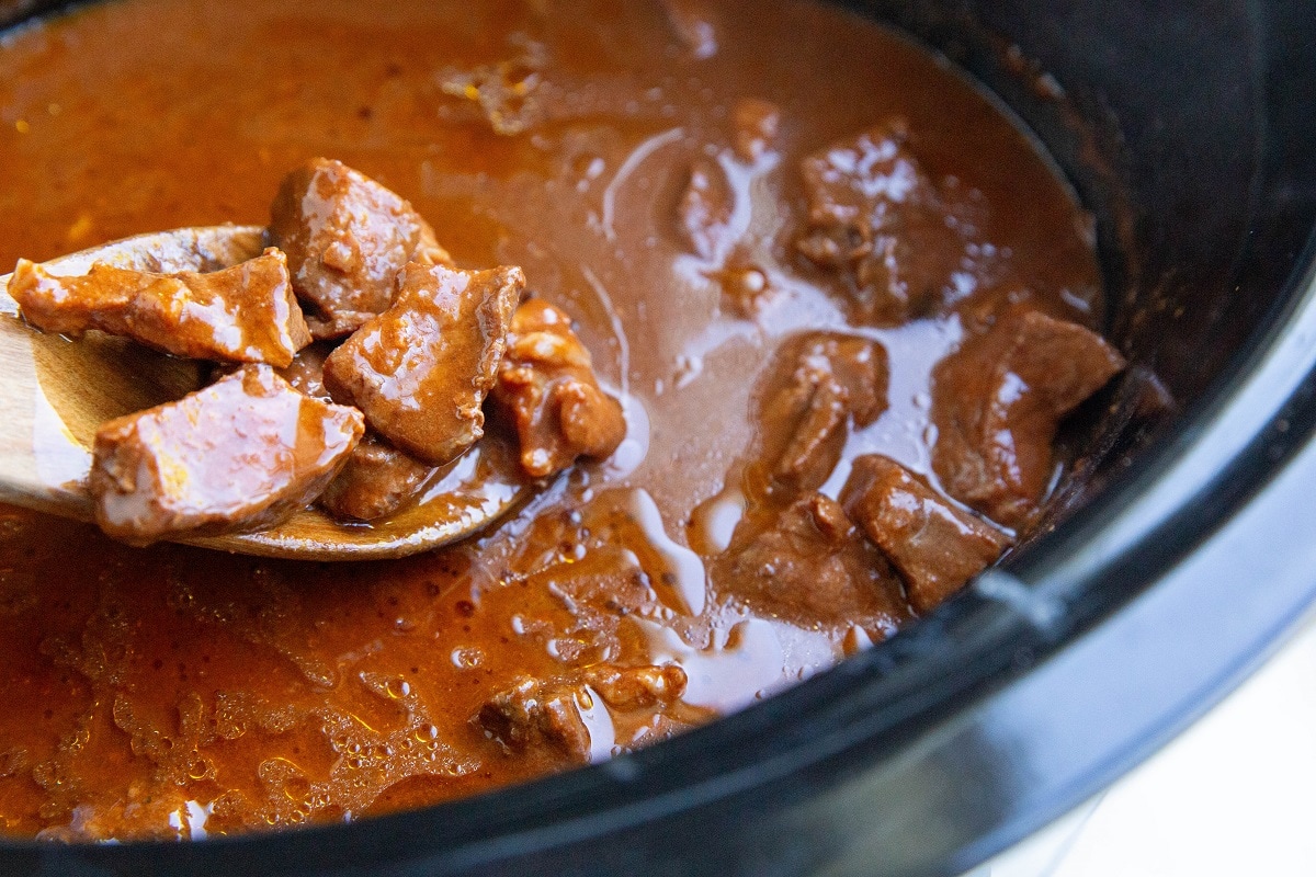 Finished chile colorado in a crock pot with a wooden spoon ladling out some of the meat.