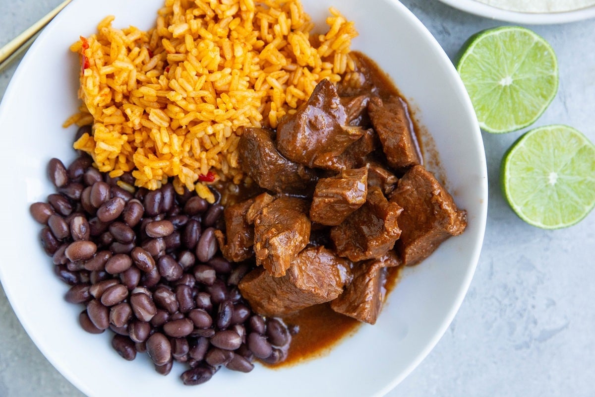 White plate with chunks of Chile Colorado, black beans, and Spanish rice.