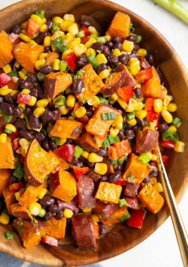 Wooden bowl of roasted sweet potato salad with a gold spoon to serve.