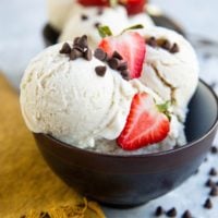 Two bowls of vanilla ice cream with chocolate chips and sliced strawberries on top.