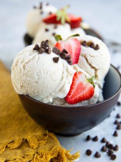 Two bowls of vanilla ice cream with chocolate chips and sliced strawberries on top.