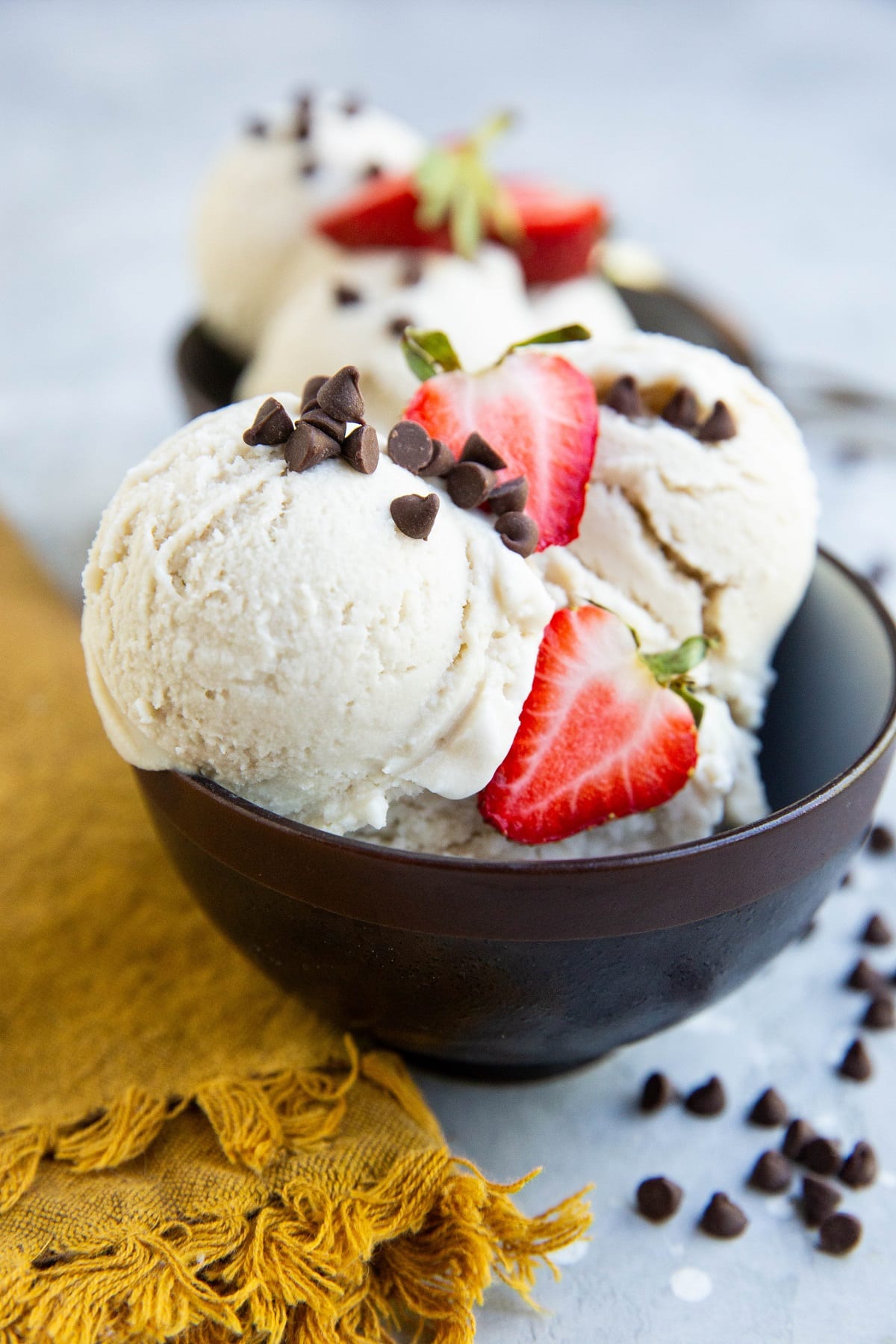 Two bowls of vanilla ice cream with chocolate chips and sliced strawberries on top.