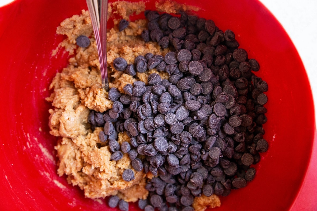 Peanut butter cookie dough in a mixing bowl with chocolate chips on top, ready to be mixed in.