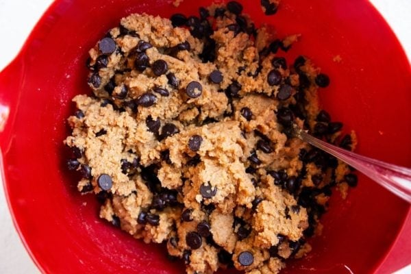 Flourless peanut butter chocolate chip cookie dough in a red mixing bowl, ready to be made into cookies.