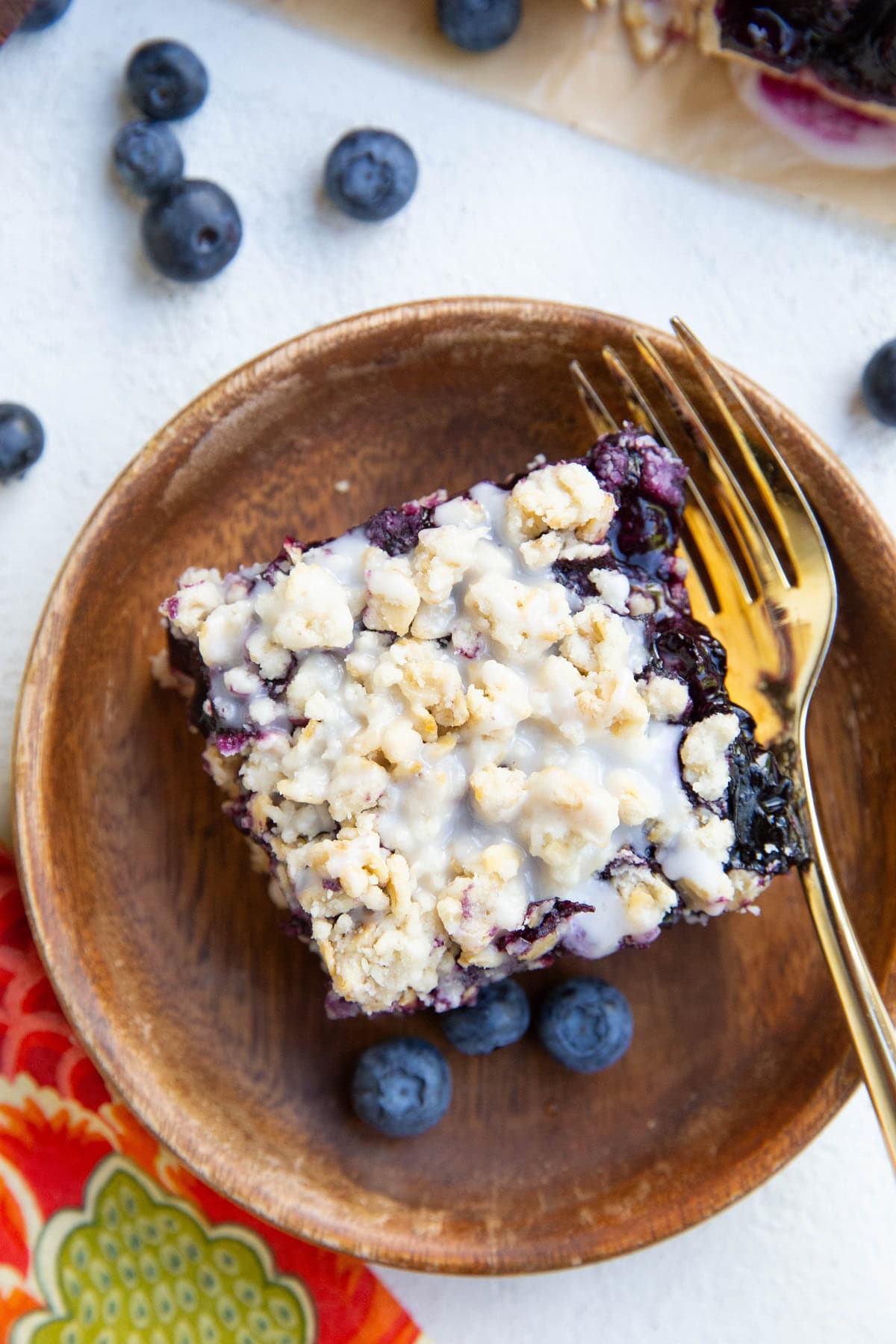 Wooden plate with a blueberry crumb bar on top. Gold fork and napkin to the side.