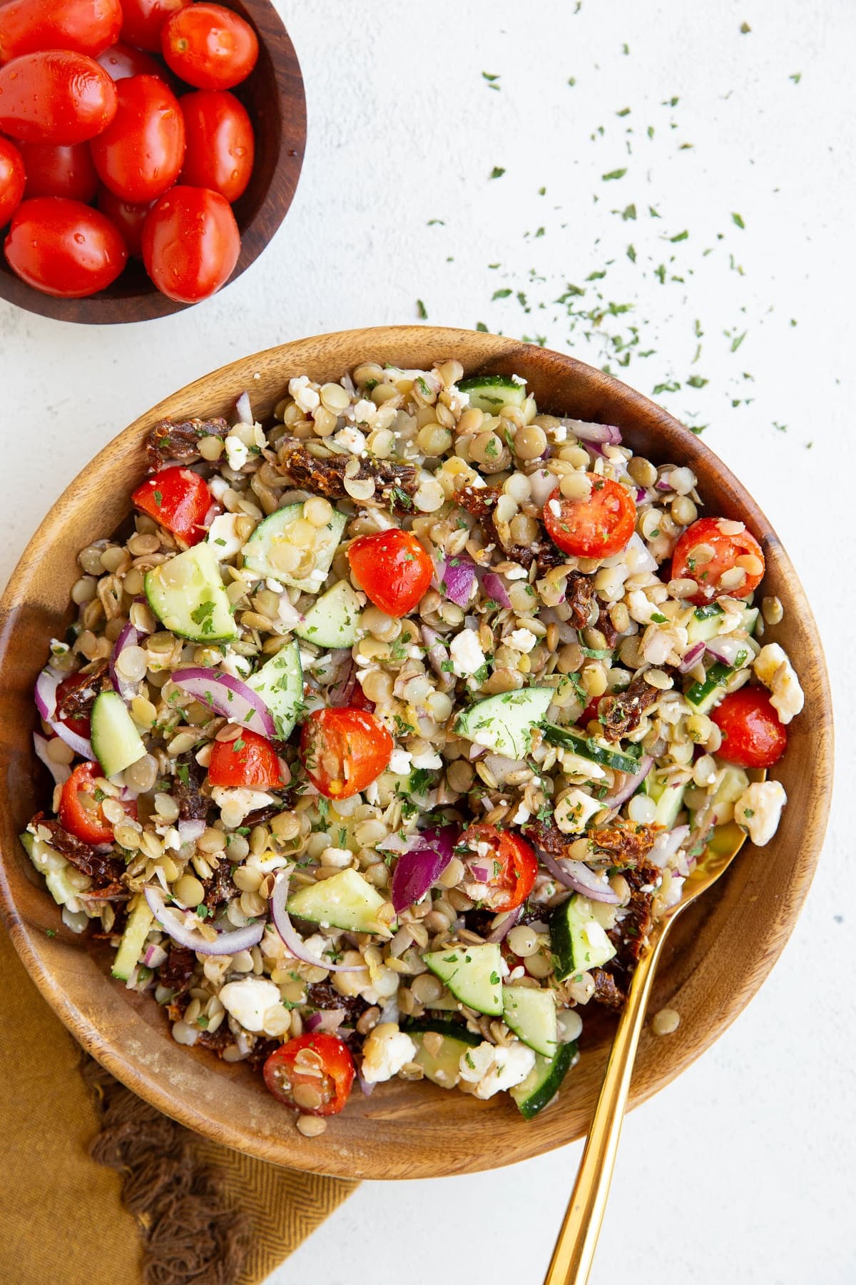 Wooden bowl of lentil salad with a golden spoon and fresh tomatoes to the side.