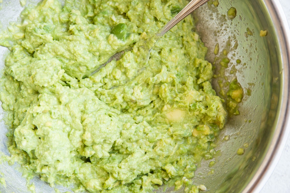 Guacamole all mashed up in a stainless steel mixing bowl with a fork.