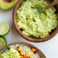 Wooden bowl of guacamole with a chicken burrito bowl to the side with guacamole on top.