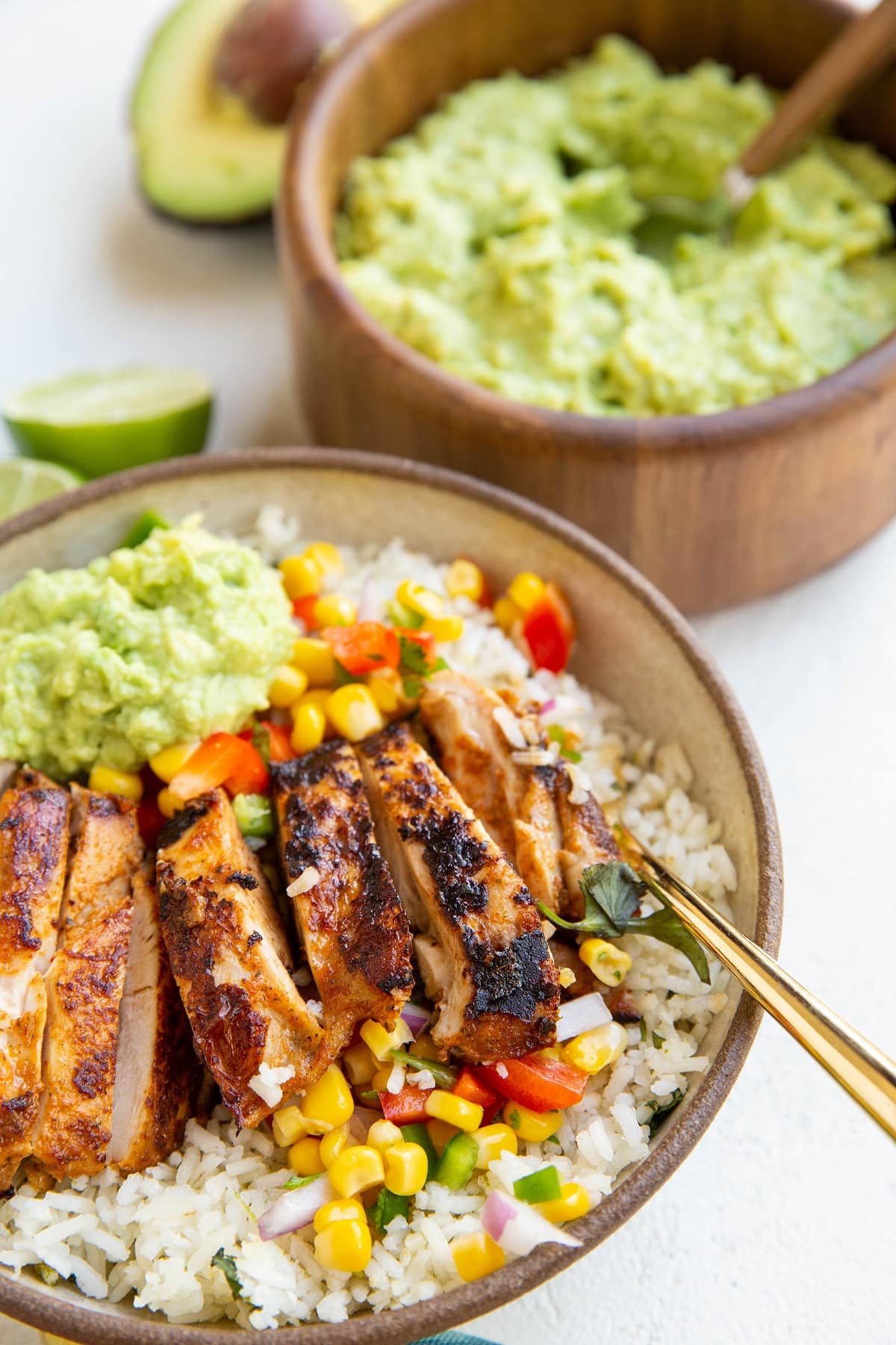 Chicken burrito bowl with guacamole on top and a bowl of guacamole behind it.