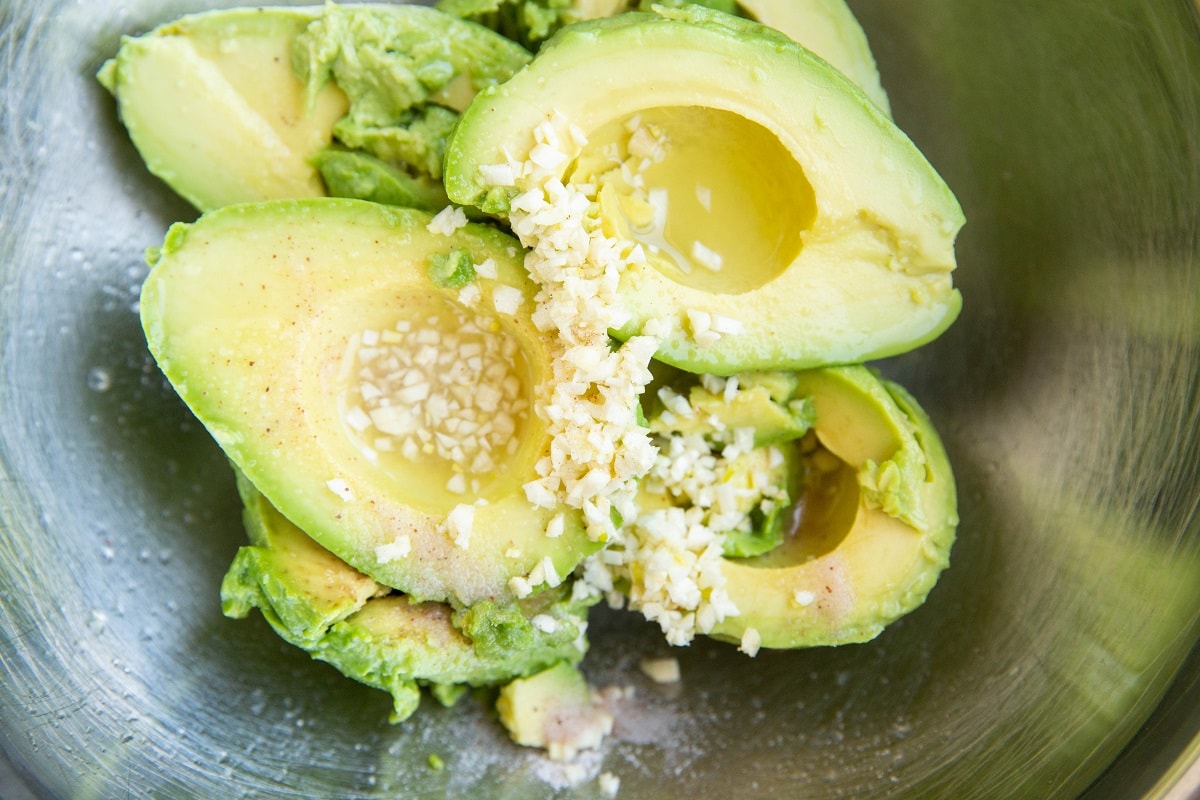 Fresh avocados, lime juice, salt, and garlic in a mixing bowl.