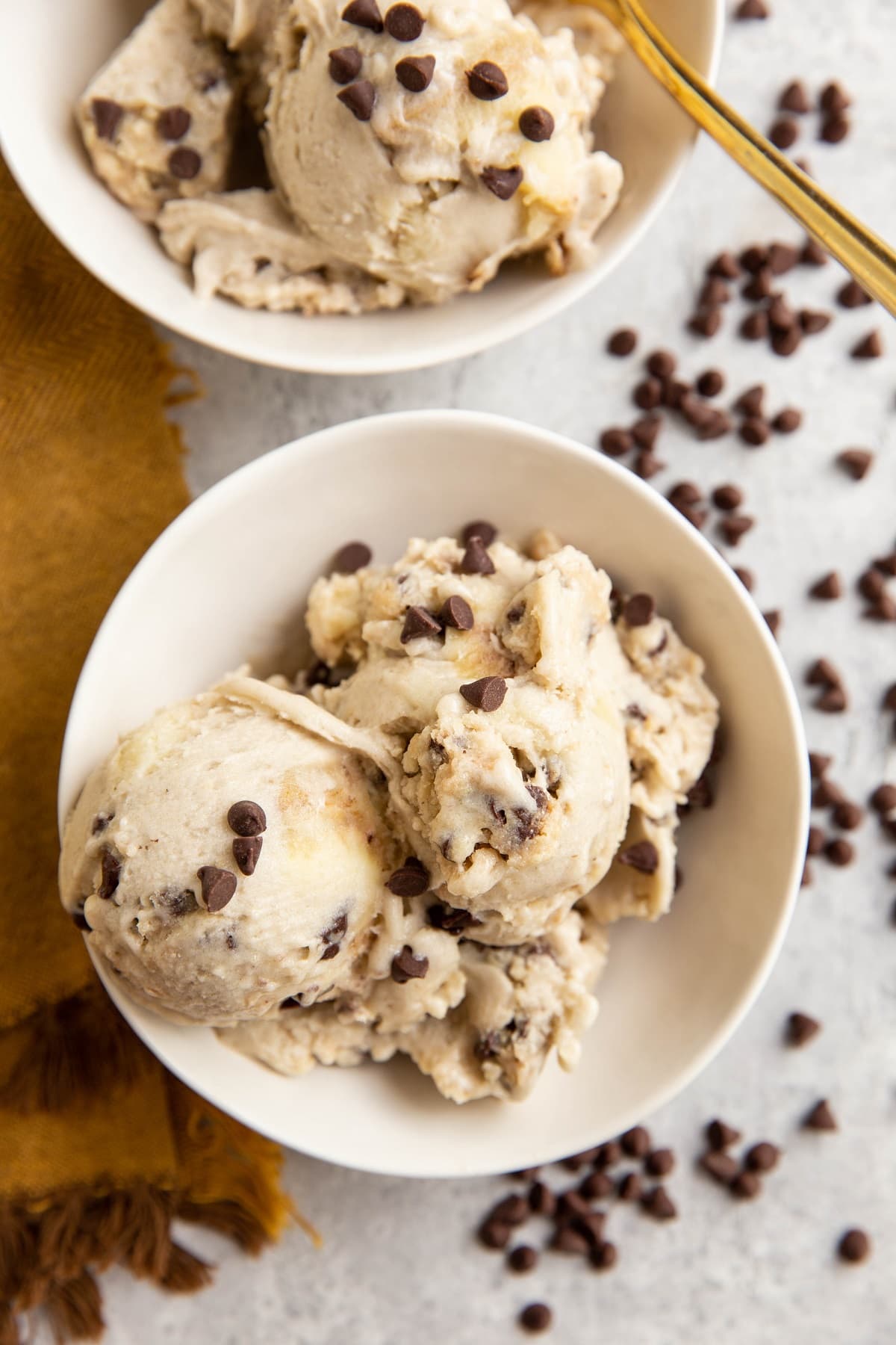 Two white bowls of cookie dough ice cream with a golden spoon.