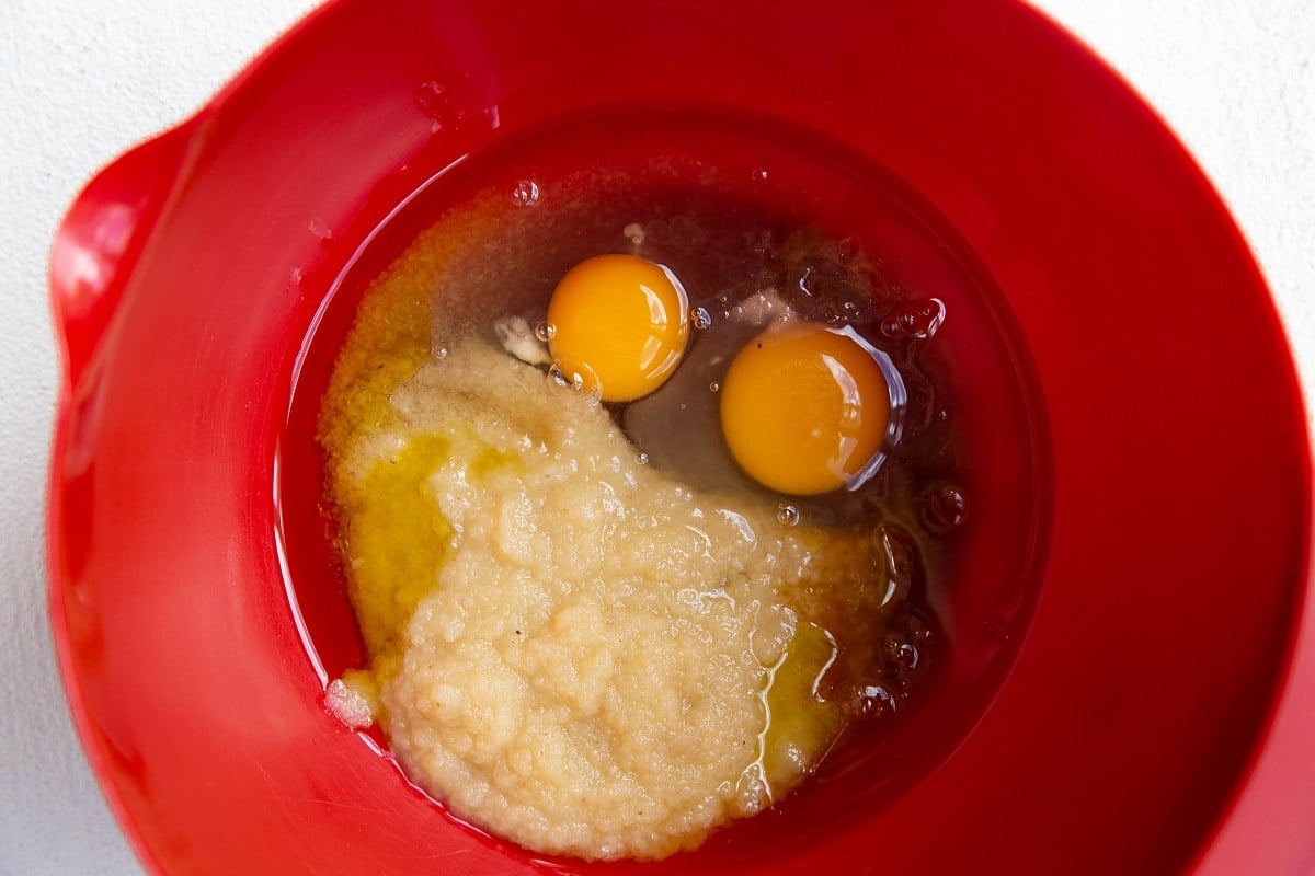 Applesauce, oil, pure maple syrup, and eggs in a red mixing bowl.