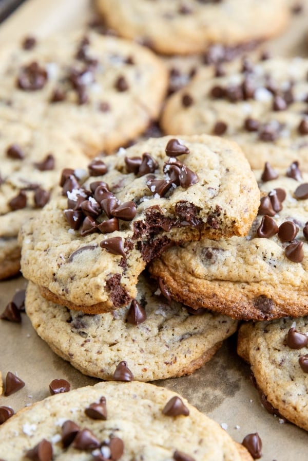 Pile of chocolate chip cookies on a baking sheet with a bite taken out of one of them.