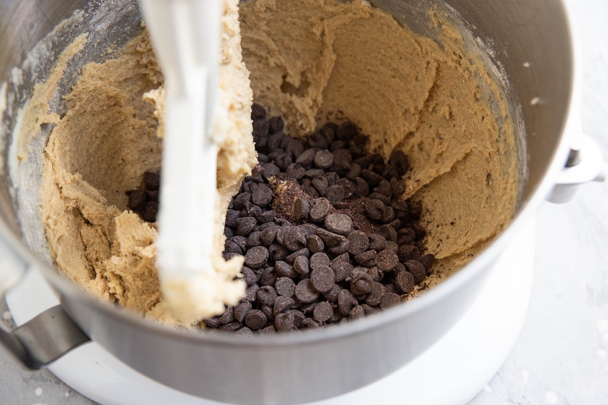 Cookie dough in a stand mixer with chocolate chips on top, ready to be mixed in.